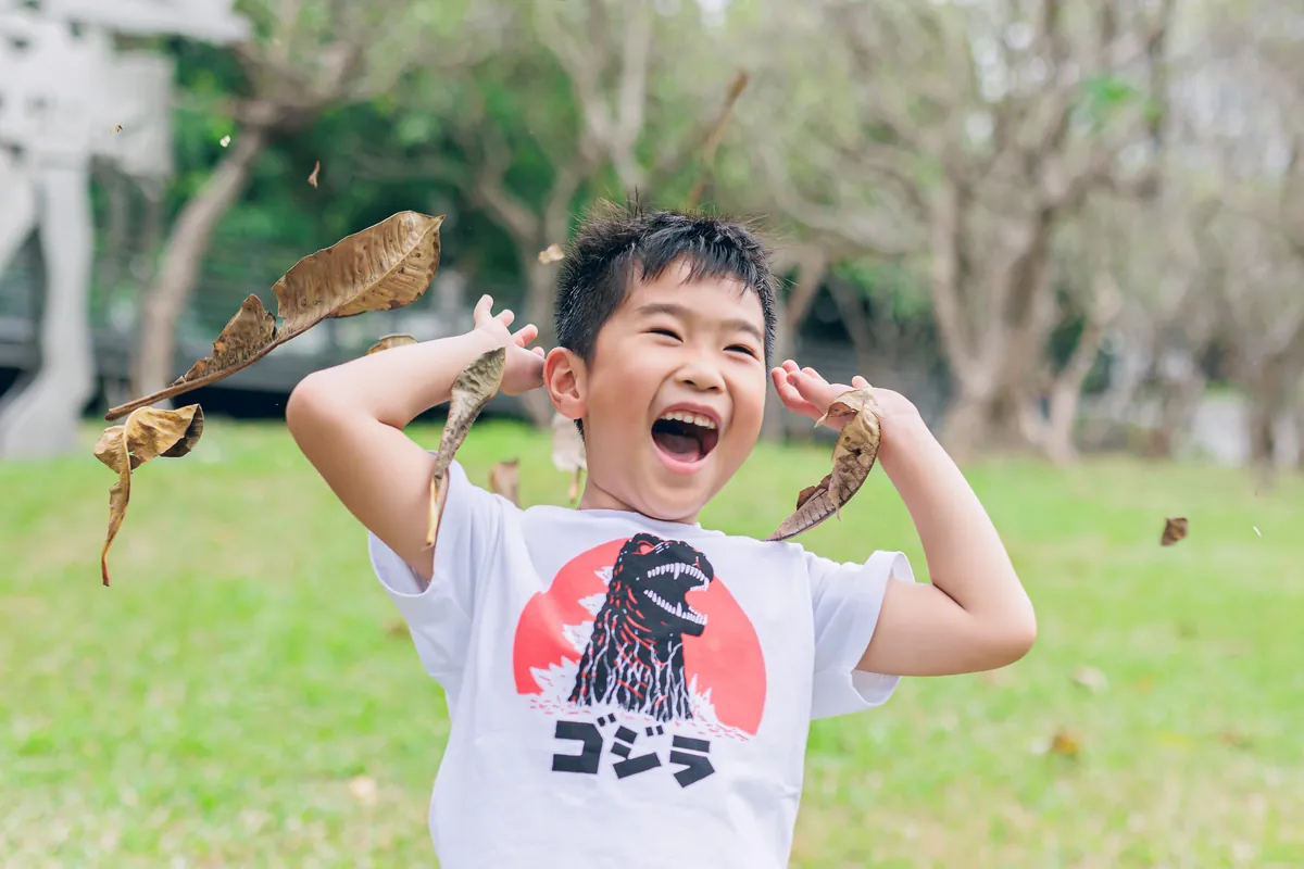 小男孩把落葉舉在頭上,做出怪獸的鬼臉